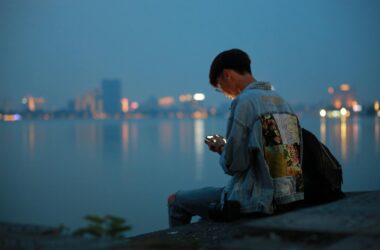 teen in denim jacket using phone by waterfront