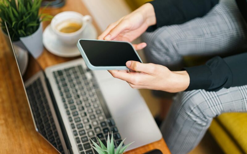 person using smartphone and laptop in office setting