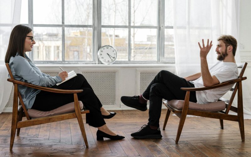 person in black pants and black shoes sitting on brown wooden chair